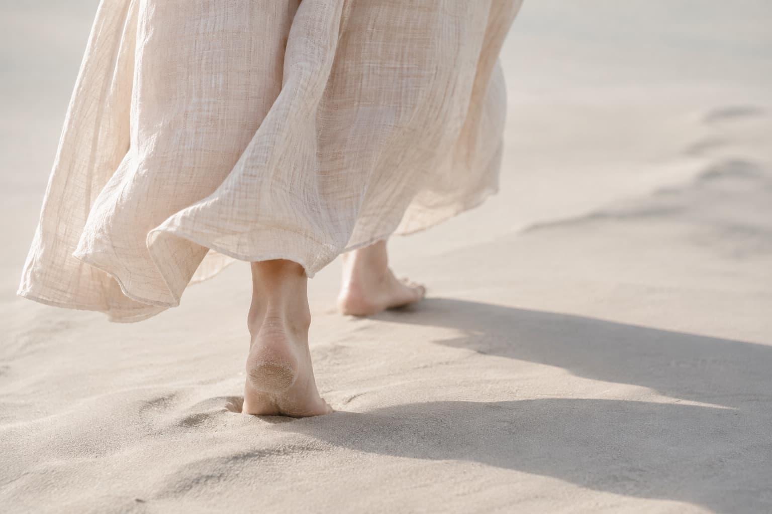 淡い砂浜を歩く女性の足元と服の裾