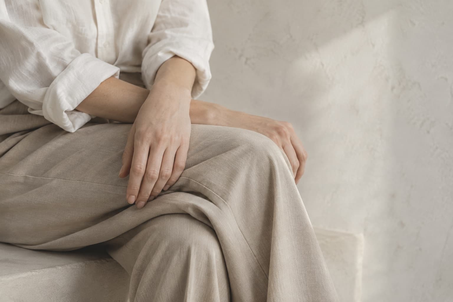 淡いベージュの服と膝に重ねた手
